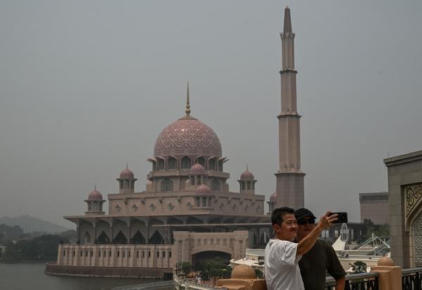 Deux personnes se prennent en photo devant une mosquée dans un air saturé par des fumées toxiques, à Putrajaya, en Malaisie, le 17 octobre 2026