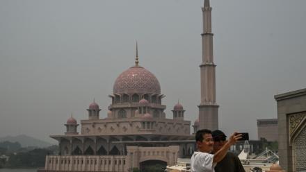 Deux personnes se prennent en photo devant une mosquée dans un air saturé par des fumées toxiques, à Putrajaya, en Malaisie, le 17 octobre 2026