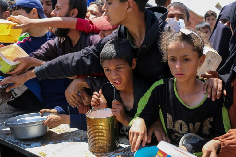 Des enfants palestiniens font la queue pour obtenir un repas chaud lors d'une distribution assurée par une cuisine soldiaire au camp de réfugiés de Nousseriat, dans le centre de la bande de Gaza, le 5 mai 2025
