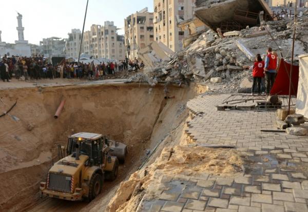 Des habitants et des membres de la Croix rouge regardent un tractopelle creuser, selon les autorités locales pour chercher les corps des otages, le 17 octobre 2025 à Khan Yunes
