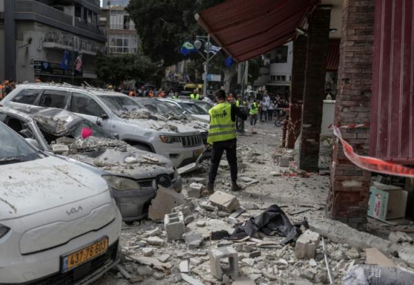 Des employés municipaux nettoient la rue devant un bâtiment touché par une attaque iranienne à Ramat Gan, dans le centre d'Israël, le 6 avril 2026