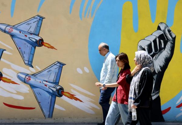 Des Iraniens passent devant des graffitis anti-américains et anti-israéliens, à Téhéran le 10 mai 2026