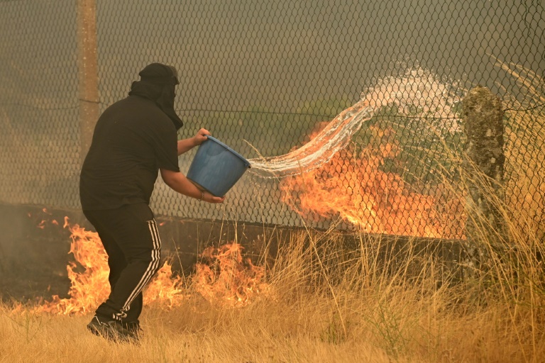 Un habitant tente de lutter contre un incendie de forêt avec un seau, dans le village de Santa Baia de Montes, province d'Ourense, dans le nord-ouest de l'Espagne, le 14 août 2025