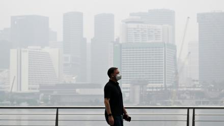 Un passant porte un masque de protection le long du boulevard à Marina Bay, noyé dans la brume, le 12 octobre 2026 à Singapour 