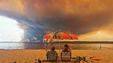 Des personnes sur la plage du Moutchic à Lacanau, dans le sud-ouest de la France, le 24 juillet 2026, tandis que des nuages de fumée d'un incendie s’élèvent dans le ciel 