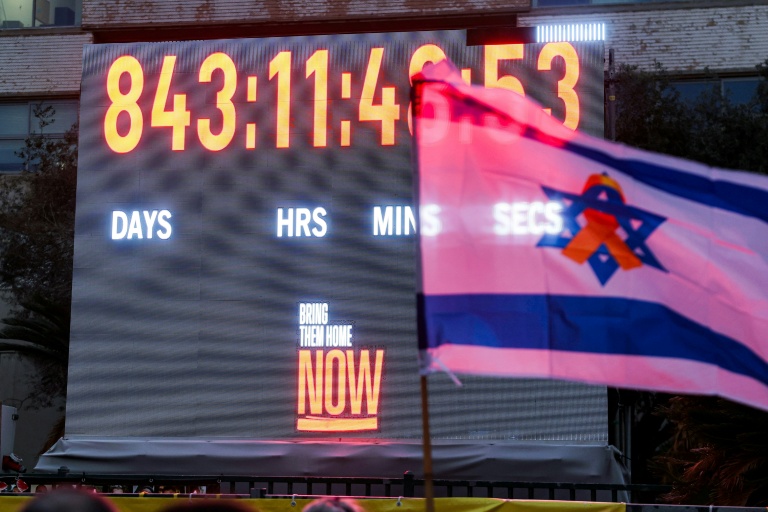 Un drapeau israélien orné d'un ruban jaune devant l'horloge comptabilisant les jours, les minutes et les secondes écoulées depuis l'enlèvement d'otages israéliens vers la bande de Gaza lors des attaques du 7 octobre 2023, à Tel-Aviv, le 27 janvier 2026