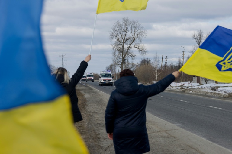 Des personnes agitent des drapeaux sur le bord  d'une route à l'approche d'un convoi de soldats libérés par les Russes après un échange de prisonniers, le 6 mars 2026 dans un lieu non précisé dans le nord de l'Ukraine