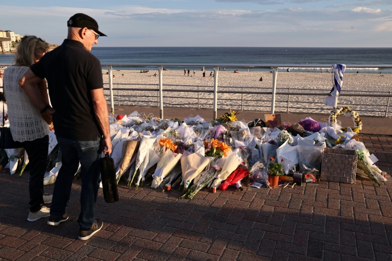 Des personnes regardent  le 20 décembre 2025 les fleurs déposées près de la plage de Bondi à la mémoire des victimes de l'attentat de Sydney