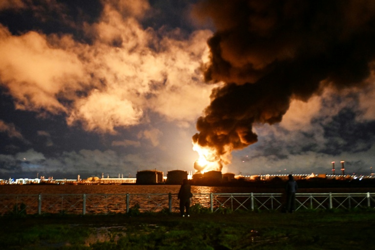 Des personnes observent un terminal pétrolier en feu à la suite d'une attaque aérienne à Saint-Pétersbourg, le 18 octobre 2026, dans le contexte du conflit russo-ukrainien en cours