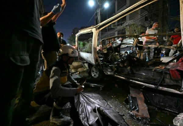 Des passants et des secouristes inspectent la carcasse du minibus dans lequel une bombe a explosé, à Jaramana, près de la capitale syrienne, Damas, le 6 août 2026