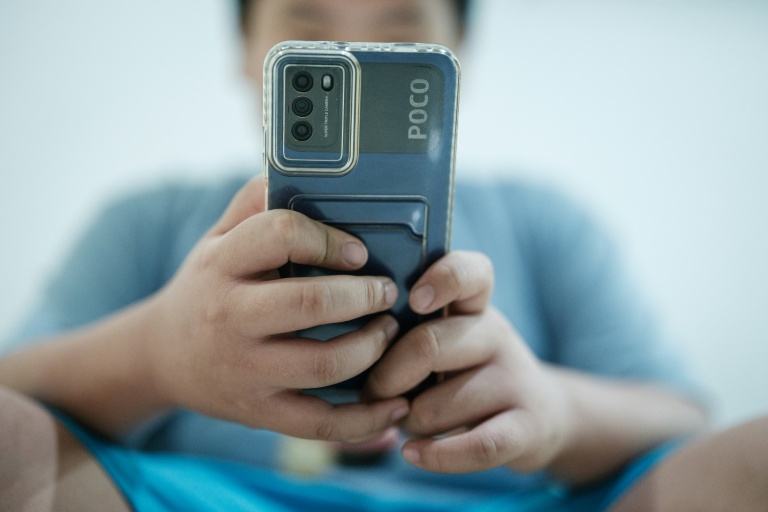 Un petit garçon regarde une vidéo sur son smartphone en attendant son père, à Jakarta, le 25 mars 2026