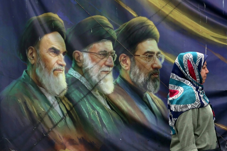 Une Iranienne passe devant les portraits des trois guides suprêmes iraniens depuis l'avènement de la République islamique, le 28 mai 2026 à Téhéran