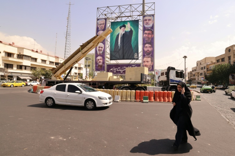 Une femme marche à côté d'un missile désactivé et devant un portrait géant du guide suprême iranien, l'ayatollah Ali Khamenei, à Téhéran le 27 septembre 2025.

