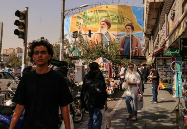 Des passants devant un panneau d'affichage représentant les dirigeants libanais du Hezbollah assassinés Hassan Nasrallah (C) et son successeur Hachem Safieddine (D), ainsi que le général iranien Qassem Soleimani, à Téhéran, le 28 septembre 2025
