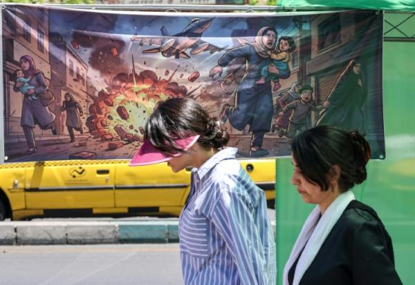 Des Iraniennes passent devant une affiche représentant les frappes israélo-américaines contre l'Iran, le 9 mai 2026 à Téhéran 