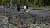 Des personnes se tiennent près d'un cratère causé par un missile, à proximité d'une école endommagée à la suite d'une attaque russe à Kiev, le 19 octobre 2026