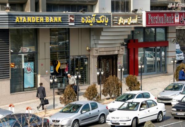 Des Iraniens passent devant une succursale de la banque Ayandeh (G) dans la capitale Téhéran, le 14 janvier 2017