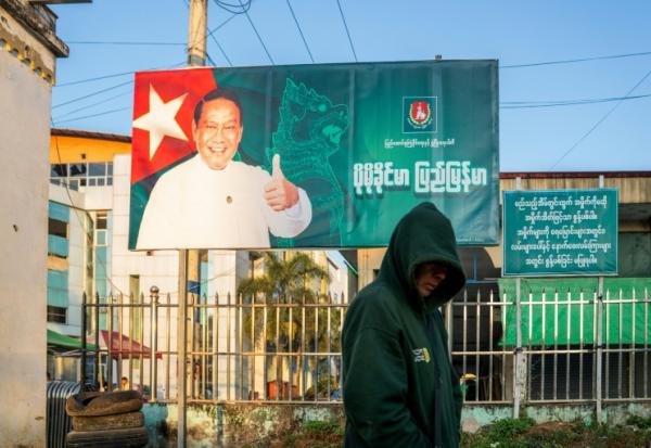Cette photo prise le 20 décembre 2025 montre un homme passer devant un panneau de campagne de Khin Yi, de l'Union pour la solidarité et le développement, dans la région de Shan en Birmanie