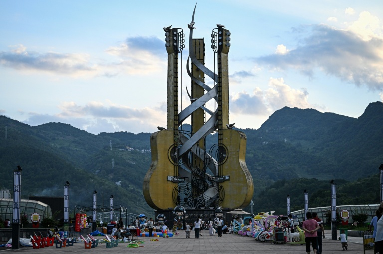 Cette photo prise le 26 juillet 2026 montre des passants devant une immense installation de guitares sur la place de la Culture de la guitare à Zheng'an, dans la province du Guizhou, dans le sud-ouest de la Chine.