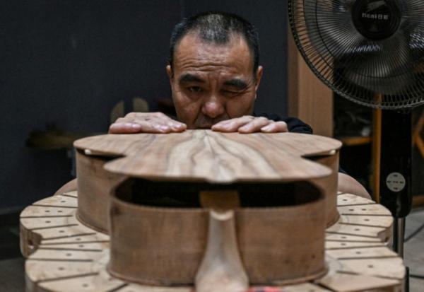 Cette photo prise le 27 juillet 2026 montre un ouvrier fabriquant une guitare dans un atelier de lutherie à Zheng'an, dans la province du Guizhou, dans le sud-ouest de la Chine.