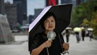 Une femme sous un parapluie avec un ventilateur portatif, le 12 juillet 2026 à Séoul 