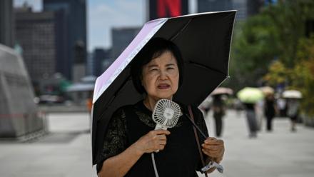 Une femme sous un parapluie avec un ventilateur portatif, le 12 juillet 2026 à Séoul 