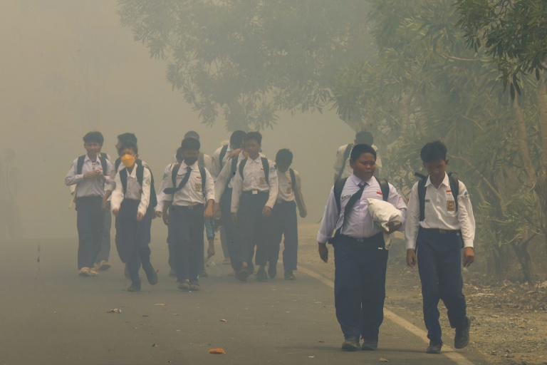 Des écoliers sur une route noyée dans une brume épaisse due aux incendies de forêt et de terres à Banjarbaru ans le Kalimantan du Sud, le 20 octobre 2026 en Indonésie