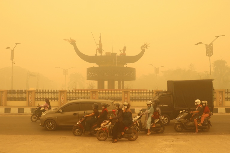 Des motocyclistes portant un masque de protection circulent dans une épaisse brume causée par des feux de forêt et de terres dans la région de Palangkaraya, dans le Kalimantan central, le 24 octobre 2026 en Indonésie