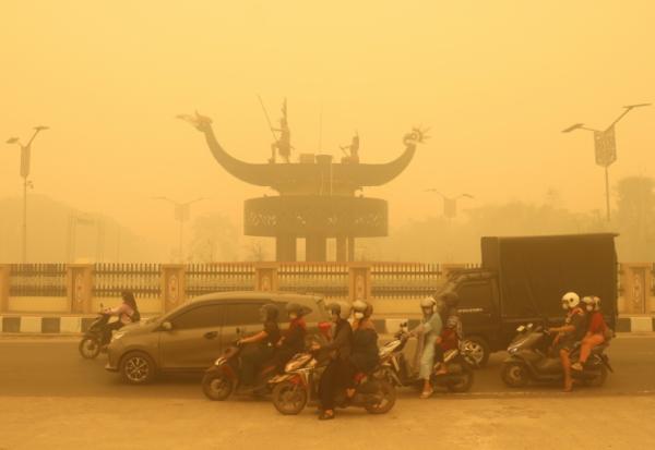 Des motocyclistes portant un masque de protection circulent dans une épaisse brume causée par des feux de forêt et de terres dans la région de Palangkaraya, dans le Kalimantan central, le 24 octobre 2026 en Indonésie