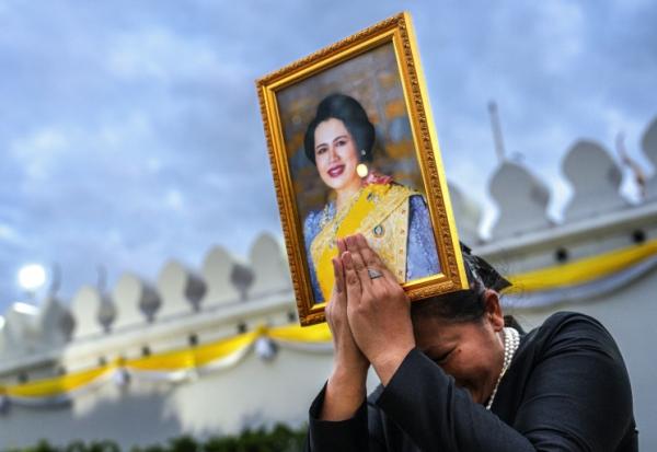 Une femme endeuillée tient un portrait de la reine mère Sirikit de Thaïlande au passage du cortège funéraire, le 26 octobre 2025 à Bangkok
