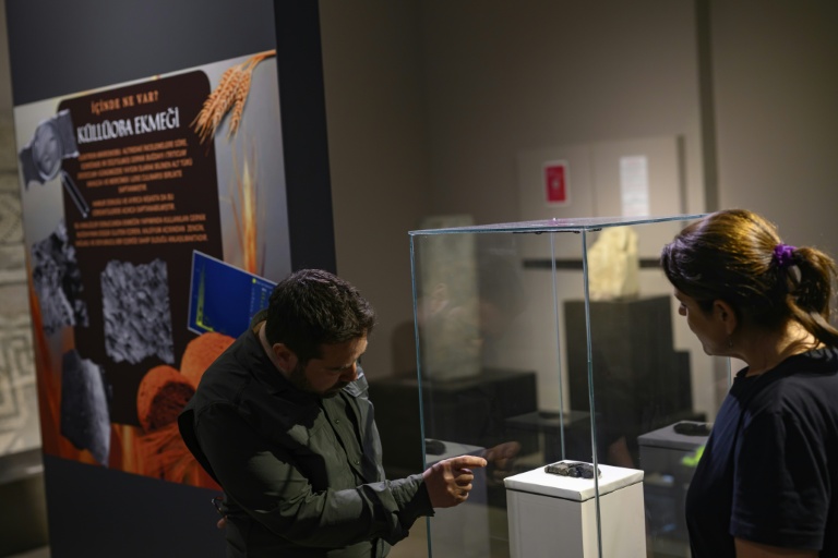 Les archéologues Murat Türkteki, à gauche, et Deniz Sari, à droite, observent un pain carbonisé vieux de 5.000 ans exposé au musée archéologique d'Eskisehir, en Turquie, le 23 mai 2025