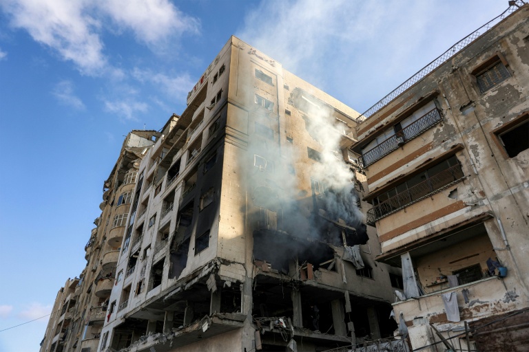 De la fumée s'échappe d'un immeuble résidentiel touché la veille par une frappe israélienne dans le quartier d'Al-Ramal à Gaza, le 16 mai 2026