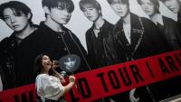 Une fan du groupe sud-coréen de K-pop BTS pose devant une affiche du groupe le 17 avril 2026 à Tokyo
