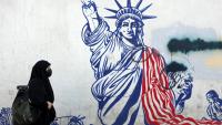 Cette photo, prise le 26 février 2026, montre une Iranienne voilée passant devant une fresque anti-américaine située à côté de l'ancienne ambassade des États-Unis à Téhéran.