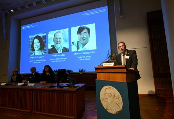 Le secrétaire général du comité Nobel Thomas Perlmann (d) près des portraits de Mary E. Brunkow, Fred Ramsdell et Shimon Sakaguchi, lauréats du Nobel de médecine, à Stockholm le 6 octobre 2025