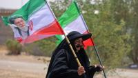 Une pèlerine iranienne brandit des drapeaux iraniens dont l'un comprend un portrait du guide suprême Ali Khamenei, tué dans un bombardement américain, le 29 juillet 2026 dans la ville-frontière de Zurbatiyah, en Irak