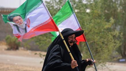 Une pèlerine iranienne brandit des drapeaux iraniens dont l'un comprend un portrait du guide suprême Ali Khamenei, tué dans un bombardement américain, le 29 juillet 2026 dans la ville-frontière de Zurbatiyah, en Irak