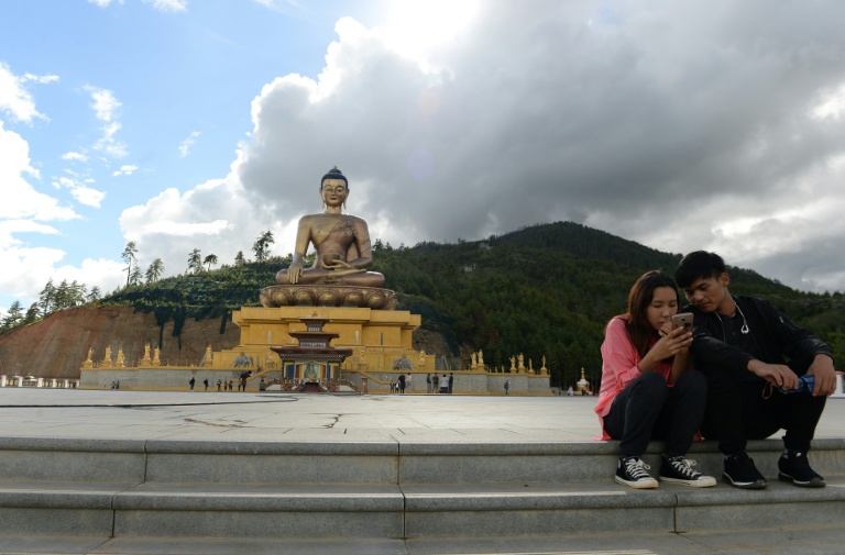 Un couple assis regarde l'écran d'un téléphone portable à côté d'une statue de Bouddha à Thimphou, la capitale du Bouthan, le  25 août 2018