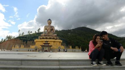 Un couple assis regarde l'écran d'un téléphone portable à côté d'une statue de Bouddha à Thimphou, la capitale du Bouthan, le  25 août 2018