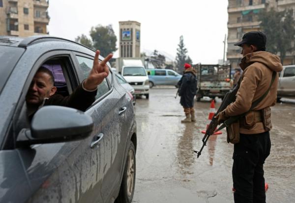 Un conducteur fait le V de la victoire en passant devant un membre des forces de syriennes, après la prise de contrôle par l'armée des quartiers kurdes d'Alep à l'issue de plusieurs jours de combats, le 11 janvier 2026