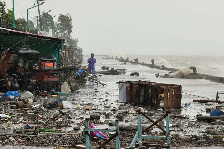 Un homme se tient à côté de débris près du bord de mer, le 22 septembre 2025 à Aparri aux Philippines