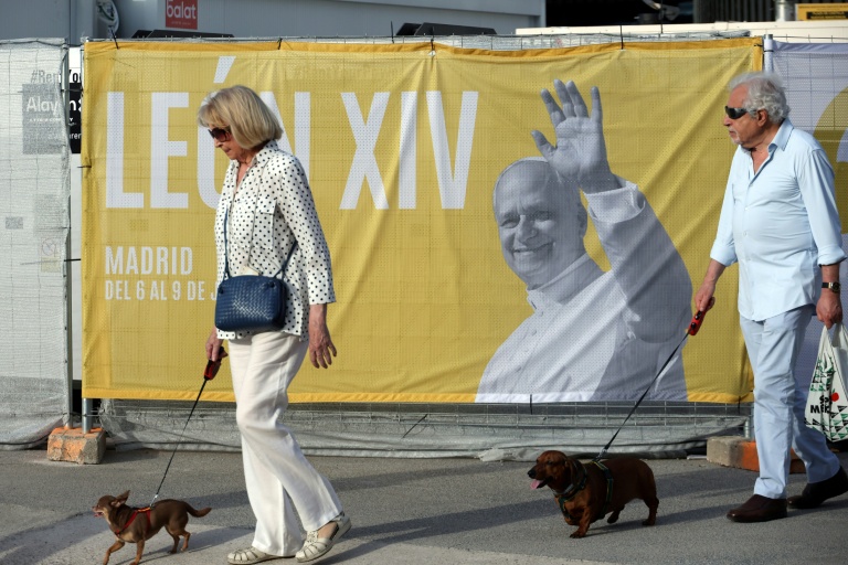 Deux personnes promènent leur chien près d'une affiche annonçant la venue du pape Léon XIV, le 5 juin 2026 à Madrid