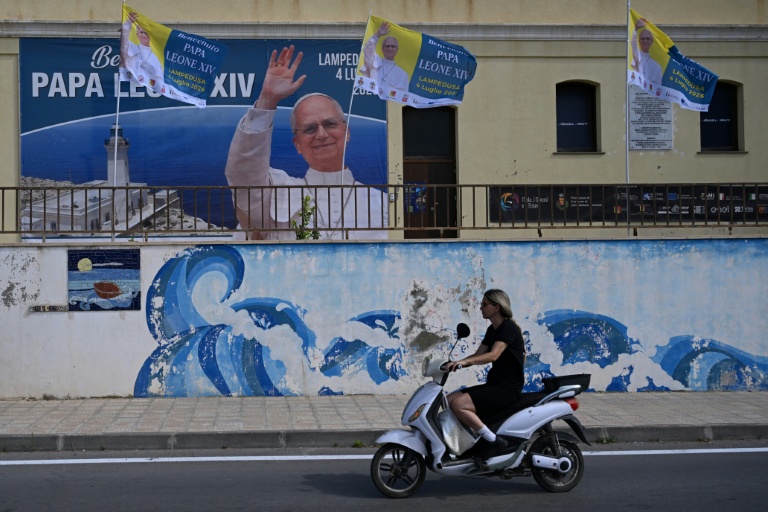 Une personne circule près d'une affiche posée pour la visite du pape Léon XIV, le 3 juillet 2026 à Lampedusa (Italie)