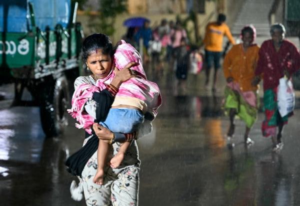 Une femme, un enfant dans les bras, se dirige vers un abri à l'approche du cyclone Arnab, le 27 octobre 2026 à Kakinada, dans l'Etat de l'Andhra Pradesh, en Inde