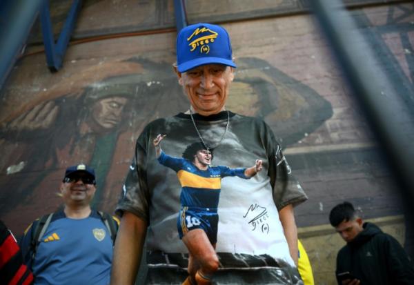 Un fan de football portant un t-shirt à l'effigie de la légende argentine Diego Maradona fait la queue devant le stade La Bombonera pour assister à la veillée funèbre de l'entraîneur argentin Miguel Angel Russo à Buenos Aires, le 9 octobre 2025. 