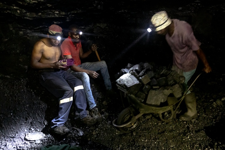 Des mineurs illégaux font une pause tandis qu'un autre pousse une brouette remplie de charbon dans la mine de Golfview à Ermelo le 25 septembre 2025, en Afrique du Sud