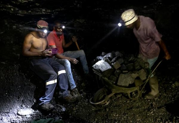 Des mineurs illégaux font une pause tandis qu'un autre pousse une brouette remplie de charbon dans la mine de Golfview à Ermelo le 25 septembre 2025, en Afrique du Sud
