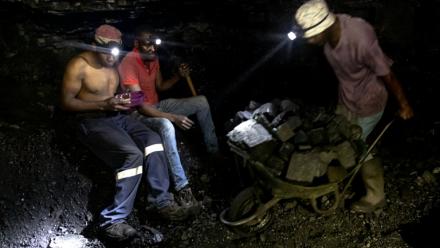 Des mineurs illégaux font une pause tandis qu'un autre pousse une brouette remplie de charbon dans la mine de Golfview à Ermelo le 25 septembre 2025, en Afrique du Sud