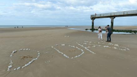 Une famille sur "Omaha Beach", où le mot "D-Day" a été tracé à l'aide de galets, à  Vierville-sur-Mer, dans le Calvados, lors des célébrations du 75e anniversaire du Débarquement en juin 2019