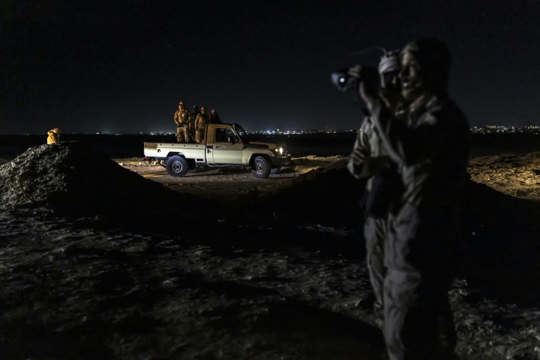 Des garde-côtes mauritaniens  utilisent des jumelles de vision nocturne pour surveiller les activités le long du littoral, tandis que d'autres se tiennent à l'arrière d'une camionnette à Nouadhibou (Mauritanie), le 23 avril 2026